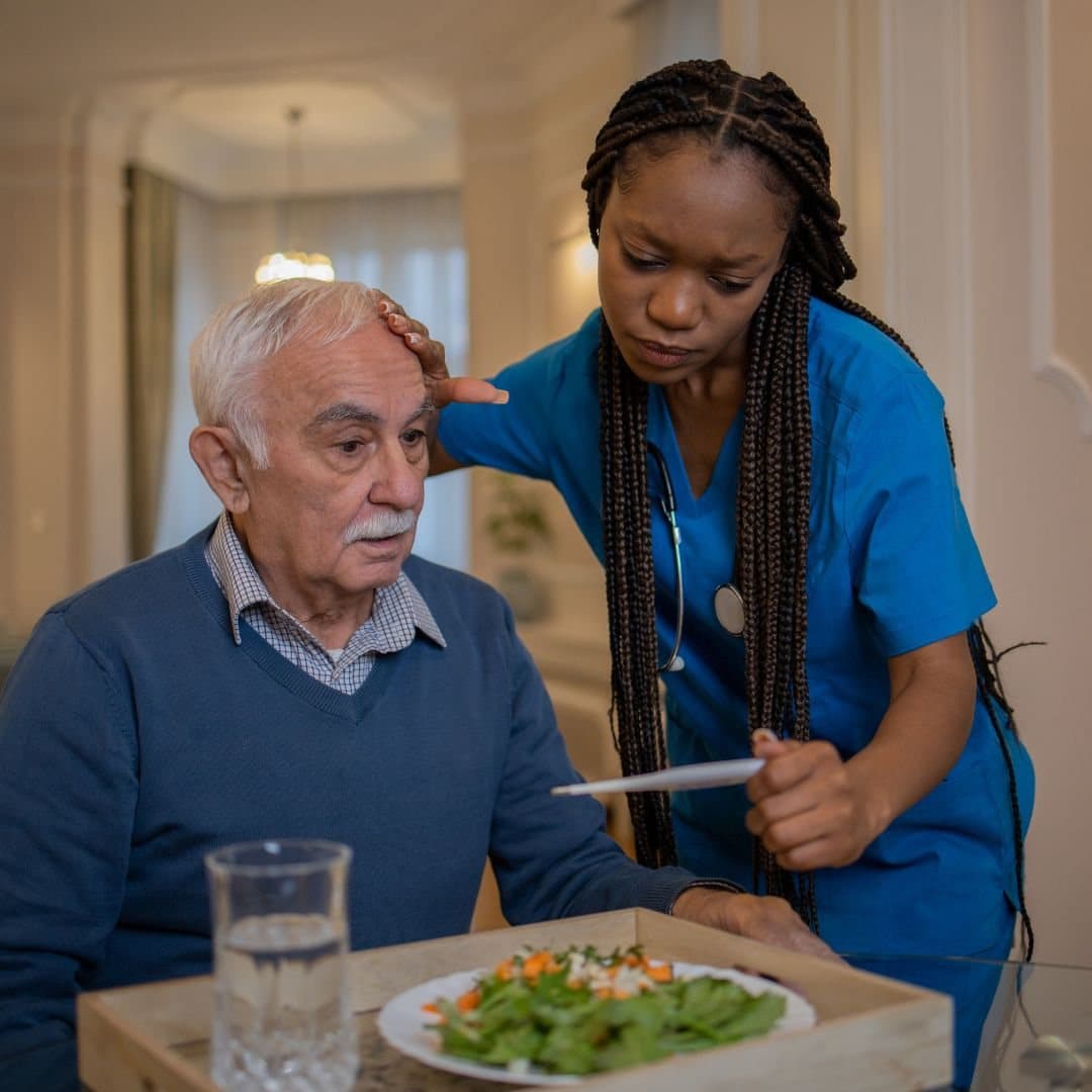 Caregiver checking on an older man during a mealtime visit